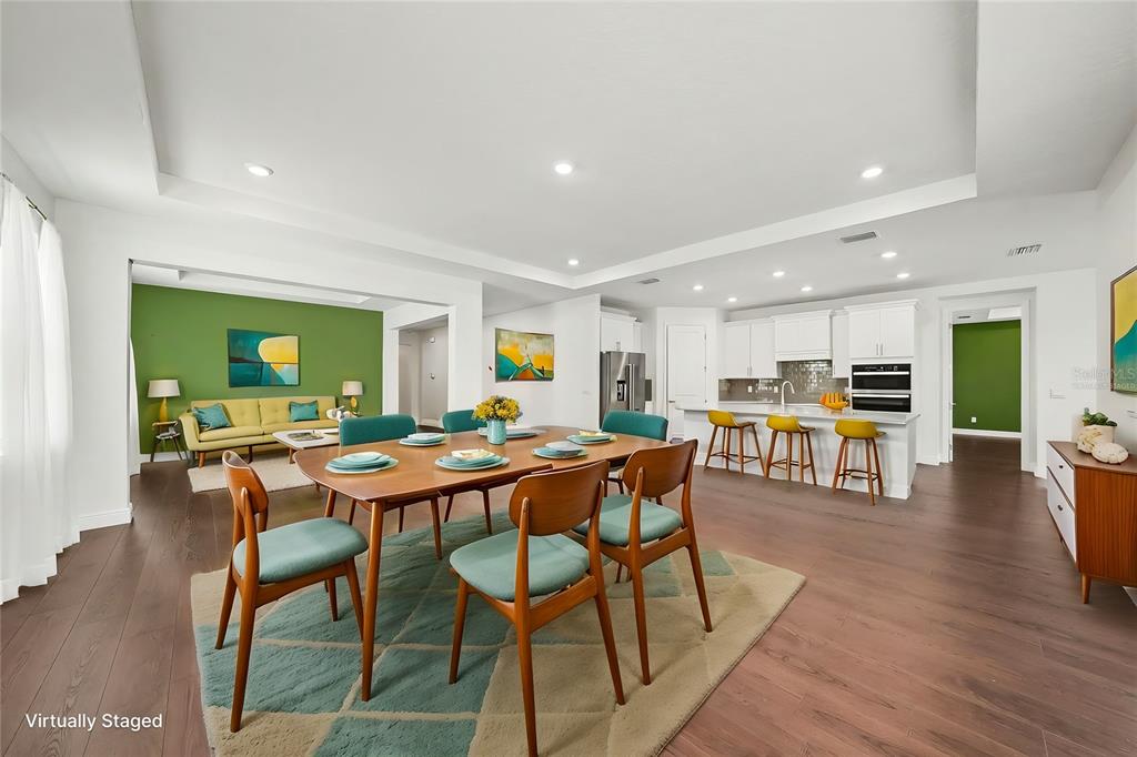 A dining area with a wooden table and chairs opens into a kitchen and living room — 23231 SCAGLIONE DRIVE, LUTZ, FL