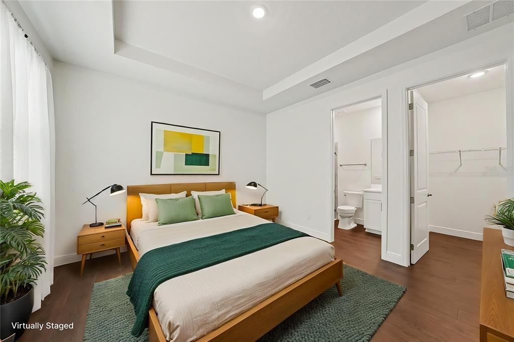A virtually staged bedroom features a wooden bed, green accents, an en-suite bathroom, and closet — 23231 SCAGLIONE DRIVE, LUTZ, FL