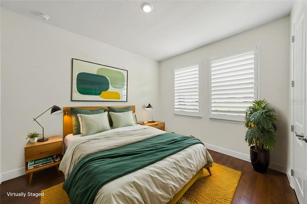 A bedroom features a bed with green bedding, a yellow rug, and white window shutters — 23231 SCAGLIONE DRIVE, LUTZ, FL