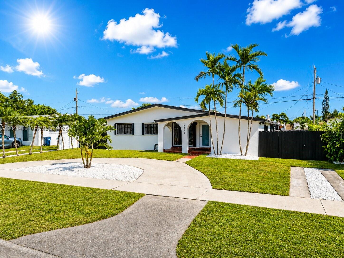 A white single-story house features a curved driveway, palm trees, and a black fence — 12370 SW 190th Ter, Miami FL 33177, MIAMI, FL