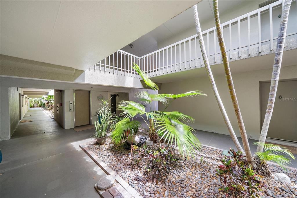 An open-air courtyard features a gravel garden with palm trees surrounded by building walkways — 3360 S OSPREY AVENUE UNIT 104B, SARASOTA, FL