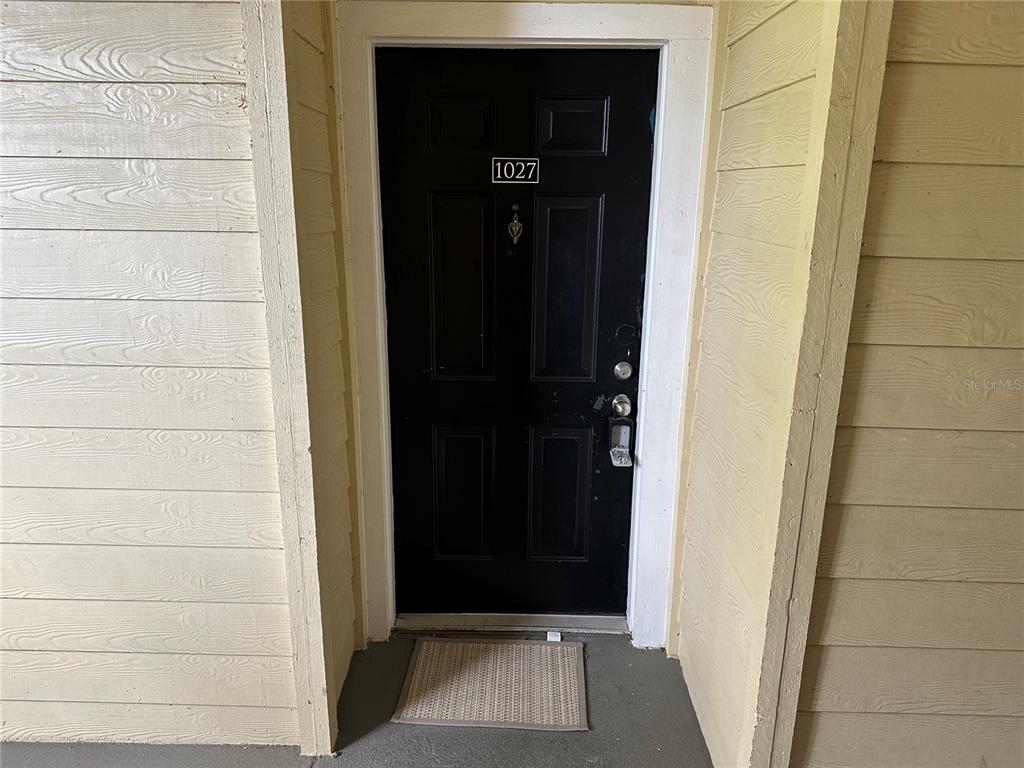 A black front door with the number 1027 is set within light-colored horizontal wood siding — 2598 ROBERT TRENT JONES DRIVE UNIT 1027, ORLANDO, FL