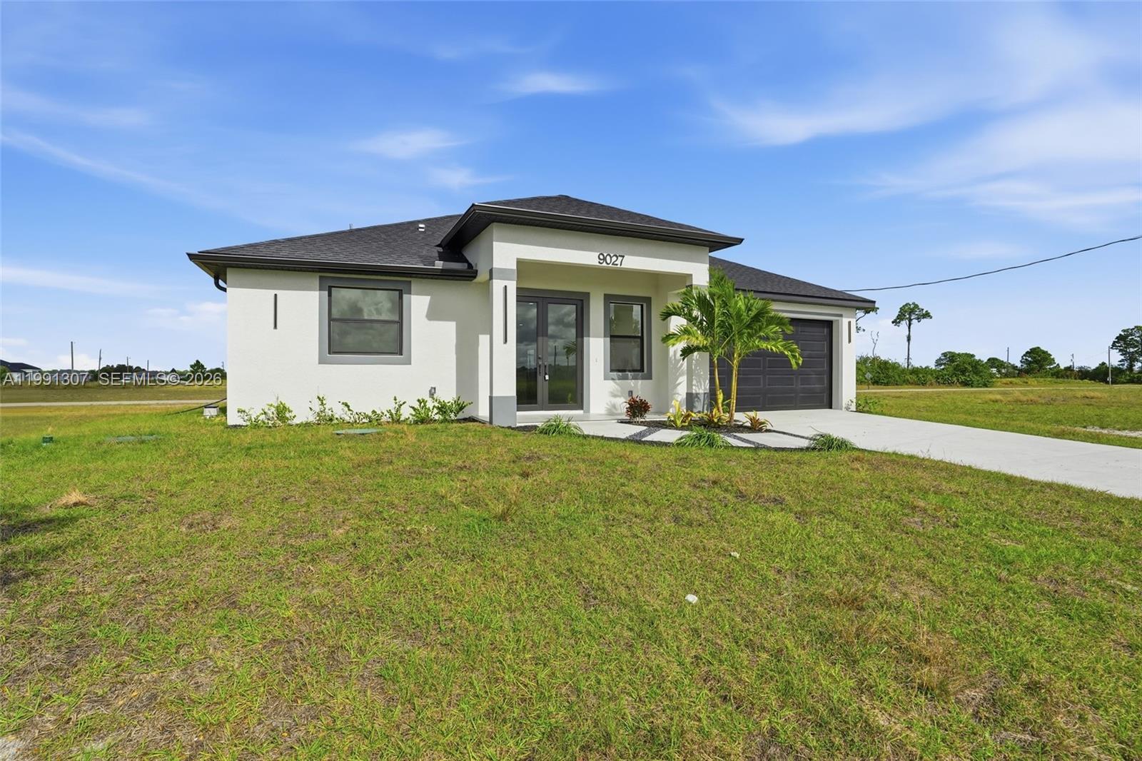 A single-story white house with a dark roof, a garage, and a front palm tree — 9027 bamboo cir, La Belle FL 33935, LA BELLE, FL