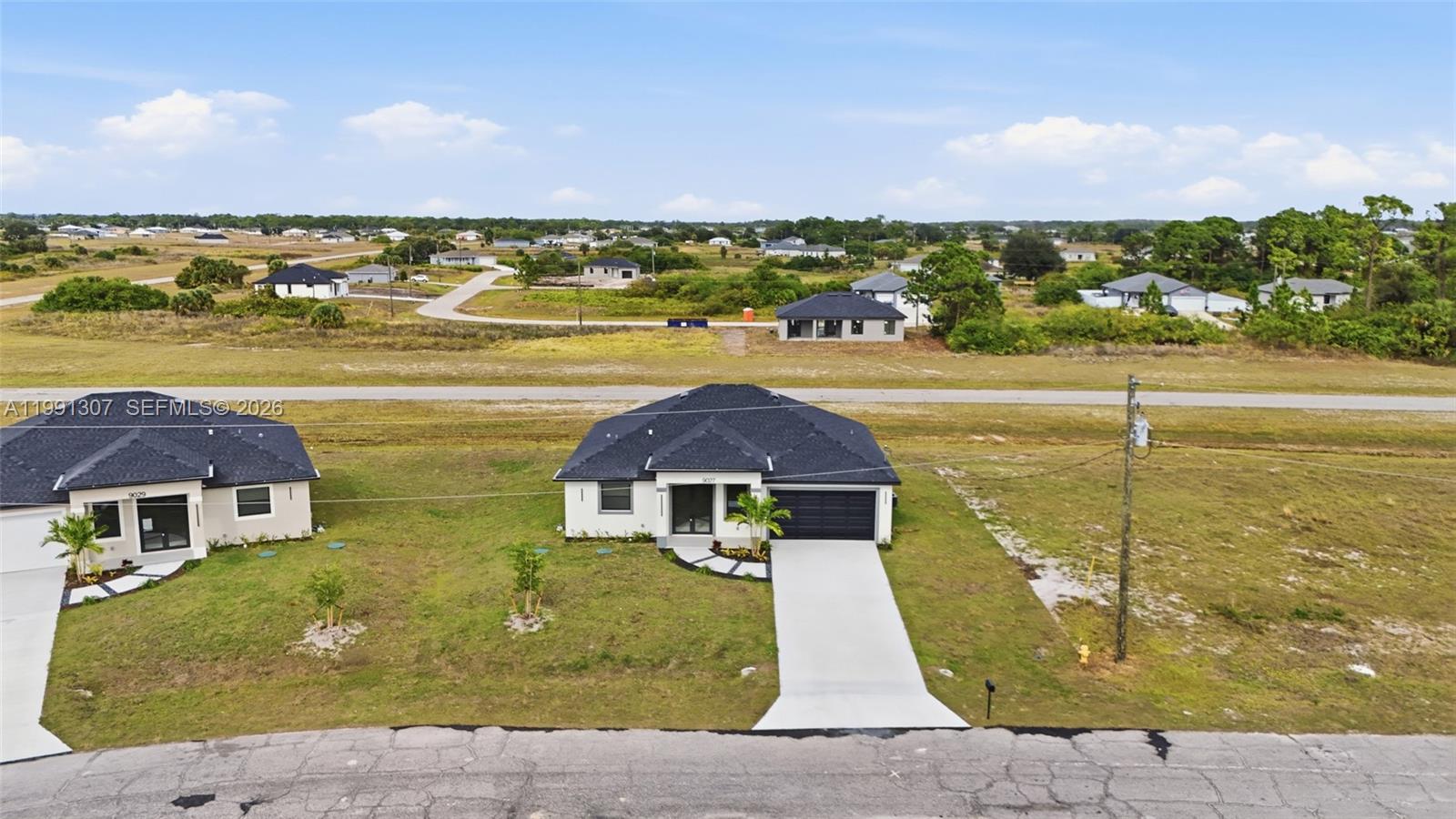 An aerial view shows two modern single-story houses with dark roofs and concrete driveways — 9027 bamboo cir, La Belle FL 33935, LA BELLE, FL