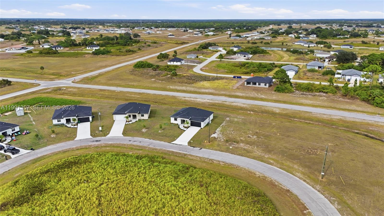 An aerial view shows three newly constructed houses along a curved road in a rural area — 9027 bamboo cir, La Belle FL 33935, LA BELLE, FL