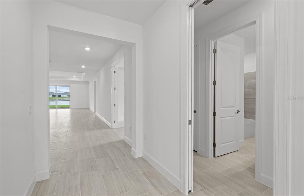 A hallway with light tile flooring leads to an open living area with water views — 16526 ENNIS PLACE, BRADENTON, FL