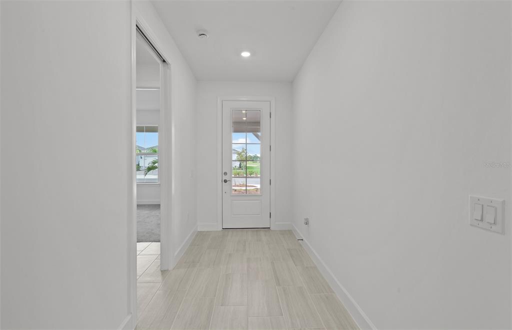 A bright hallway features light-colored tile flooring, white walls, and a glass-paneled exterior door — 16526 ENNIS PLACE, BRADENTON, FL