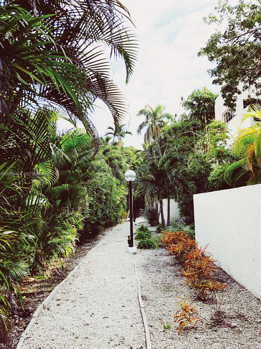 A gravel path leads through a lush tropical garden with palm trees and a lamppost — MIAMI, FL