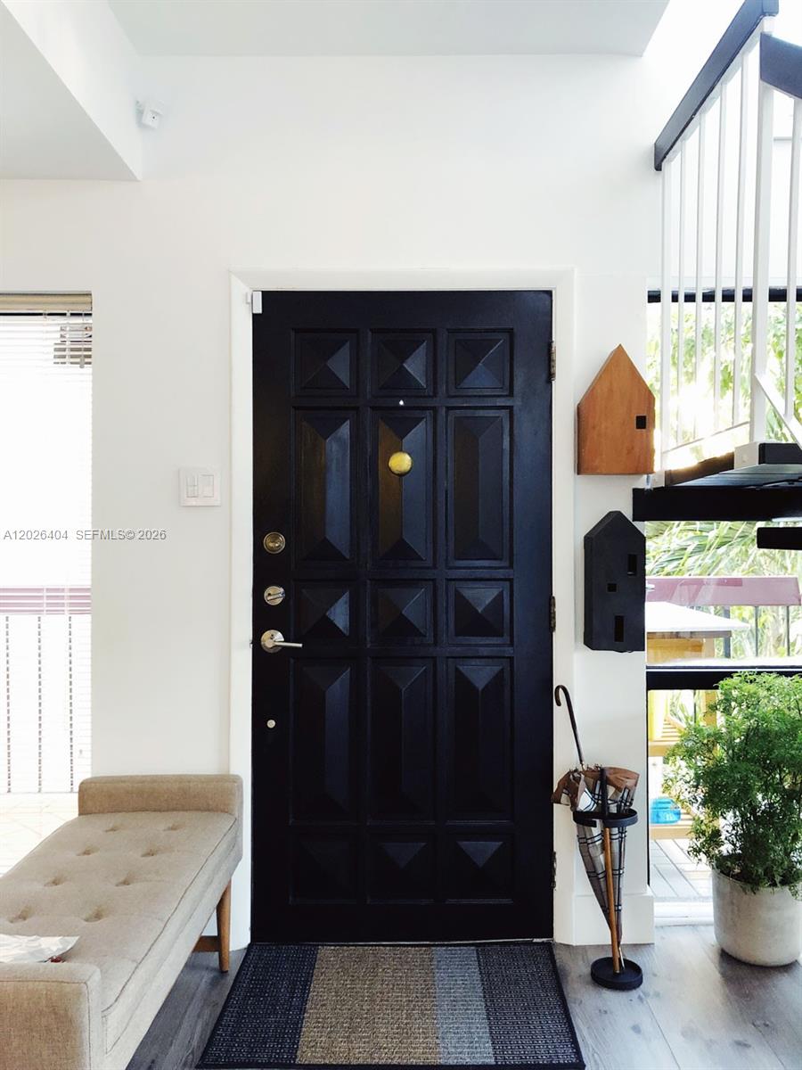 A black front door with a gold knocker stands in a bright entryway with stairs — MIAMI, FL