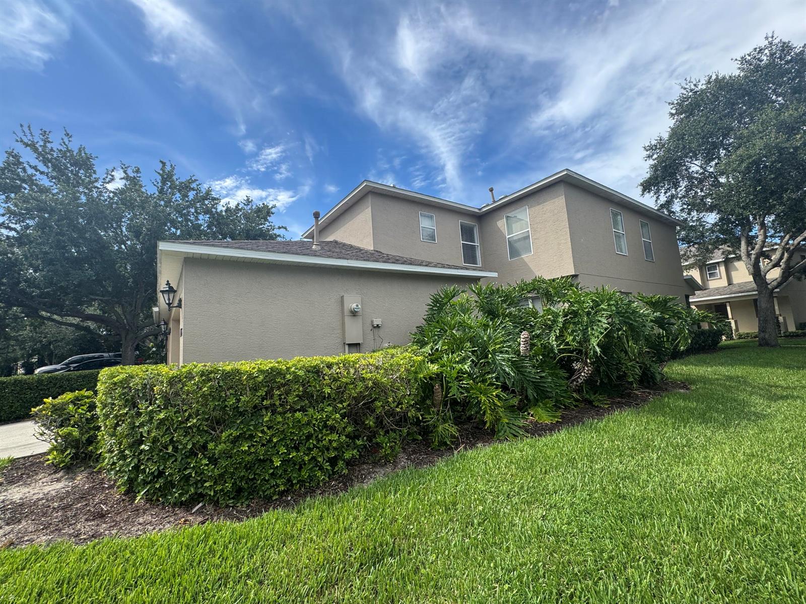 A two-story tan stucco house with a manicured hedge and large tropical plants — 1733 Pointe West Way, Vero Beach FL 32966, VERO BEACH, FL