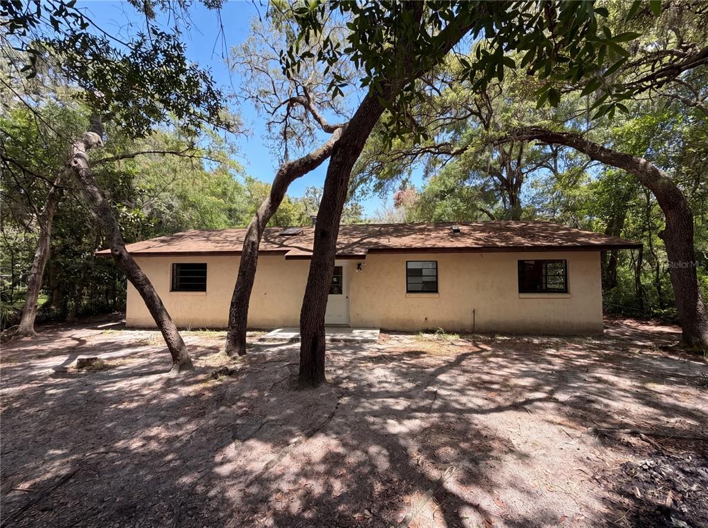 A single-story house with a tan stucco exterior sits in a wooded, sandy yard — 2505 VELMA TERRACE, LEESBURG, FL