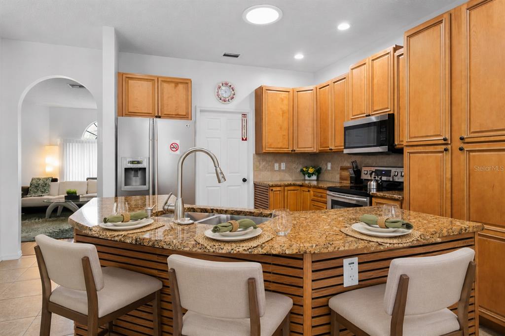 A kitchen features a curved granite island with three chairs and light wood cabinetry — 11426 ZENITH CIRCLE, TAMPA, FL