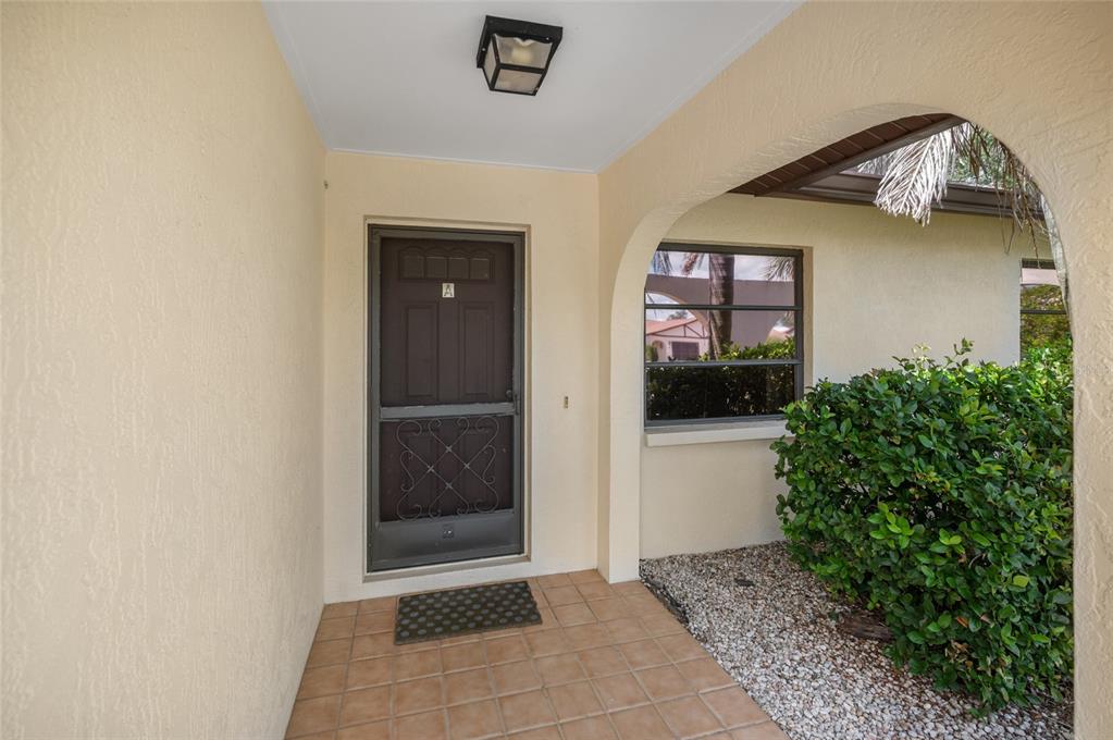 A covered entryway features a tiled floor, a dark storm door, and a nearby window — 221 HIGH POINT DRIVE UNIT 221A, ENGLEWOOD, FL