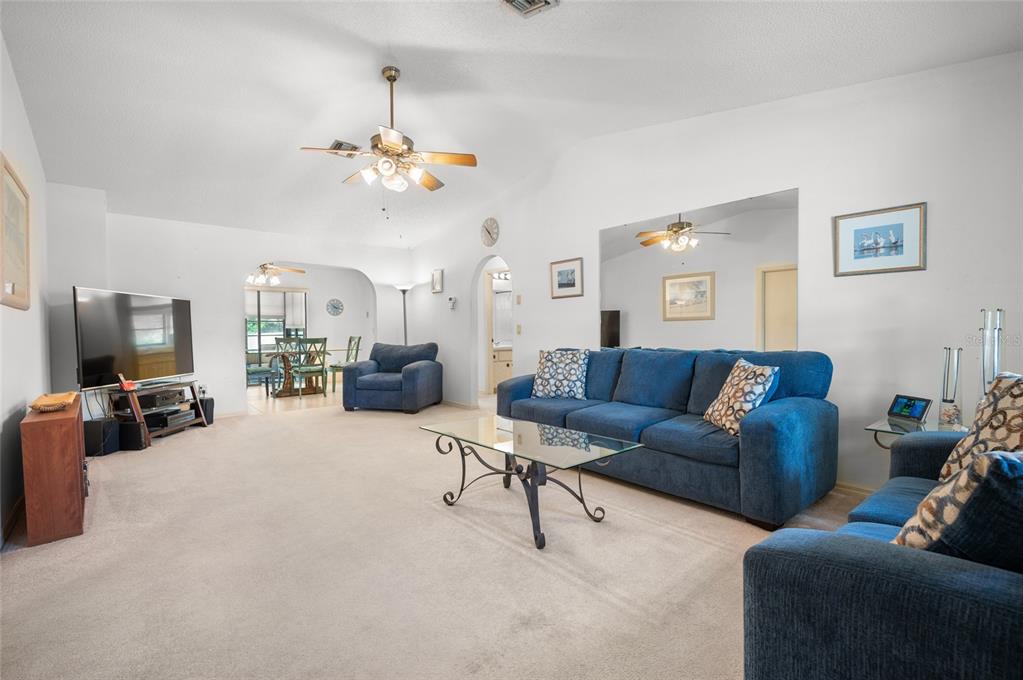 A living room features blue sofas, a glass coffee table, and beige wall-to-wall carpeting — 221 HIGH POINT DRIVE UNIT 221A, ENGLEWOOD, FL