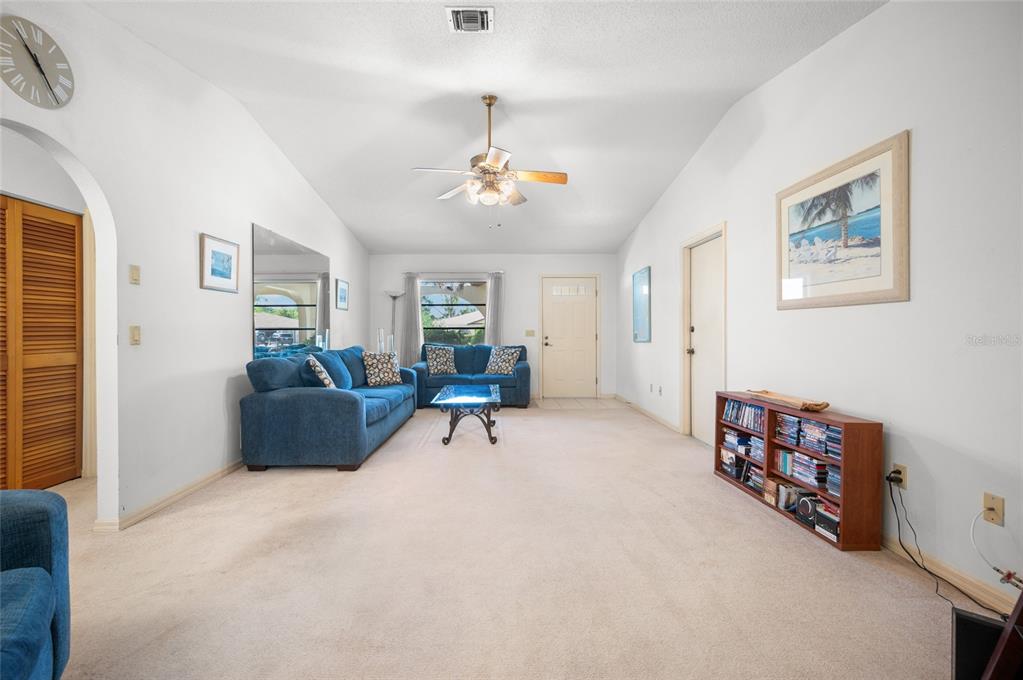 A living room features blue sofas, a ceiling fan, a bookshelf, and beige carpeting — 221 HIGH POINT DRIVE UNIT 221A, ENGLEWOOD, FL