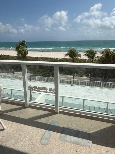 A balcony view overlooking a paved patio, palm trees, a sandy beach, and the ocean — 5601 Collins Ave # 505, Miami Beach FL 33140, MIAMI BEACH, FL