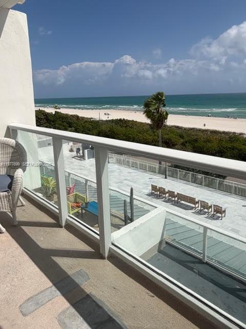 A balcony with a glass railing overlooks a beach, ocean, and a patio with chairs — 5601 Collins Ave # 505, Miami Beach FL 33140, MIAMI BEACH, FL