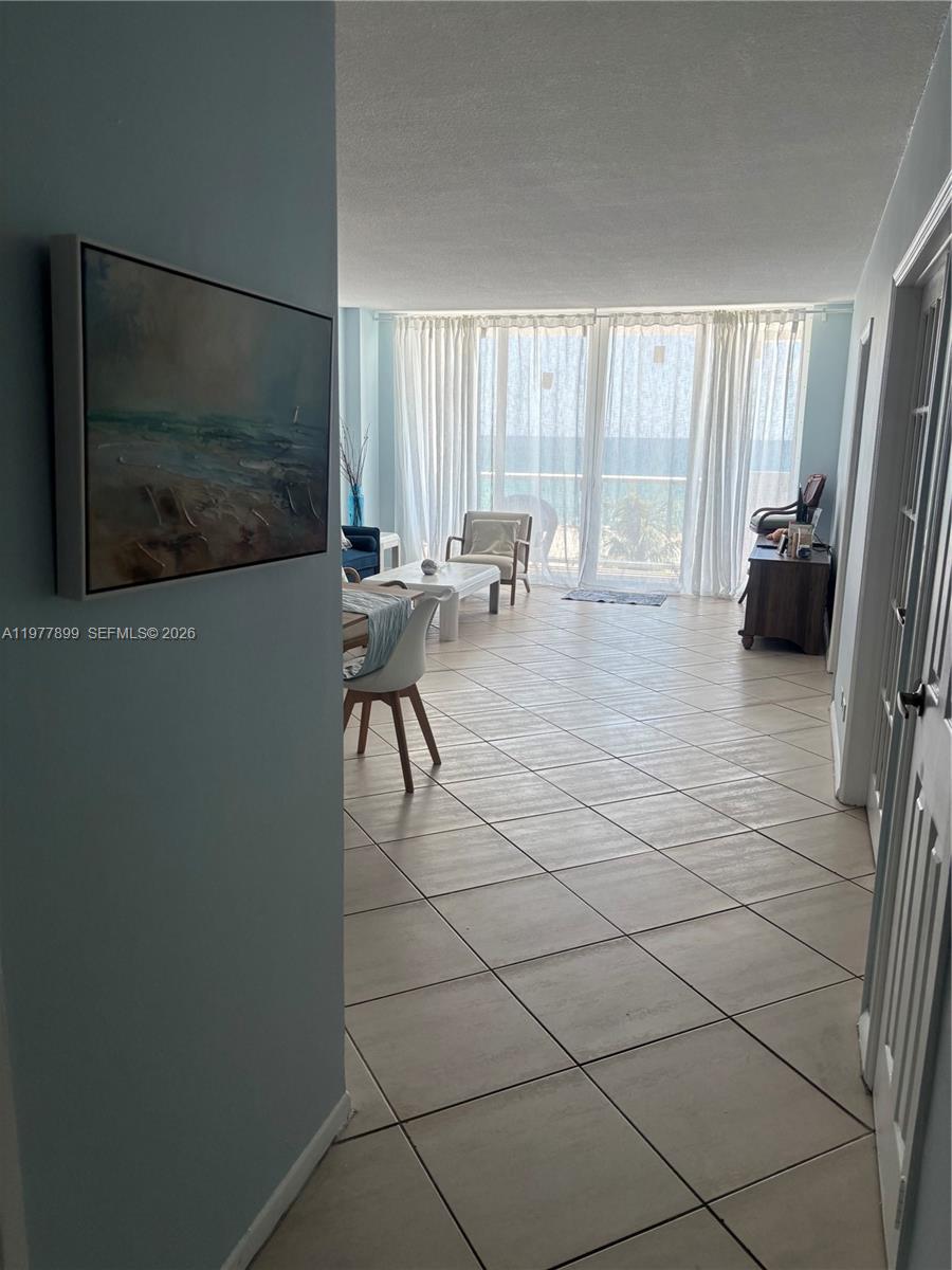 A tiled living area leads to a balcony with ocean views through floor-to-ceiling curtains — 5601 Collins Ave # 505, Miami Beach FL 33140, MIAMI BEACH, FL