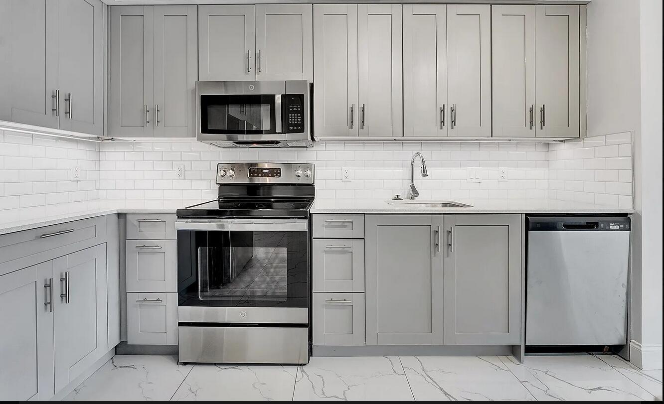A modern kitchen features gray shaker cabinets, stainless steel appliances, white subway tile, and marble flooring — 100 W Hidden Valley Boulevard # 302, Boca Raton FL 33487, BOCA RATON, FL
