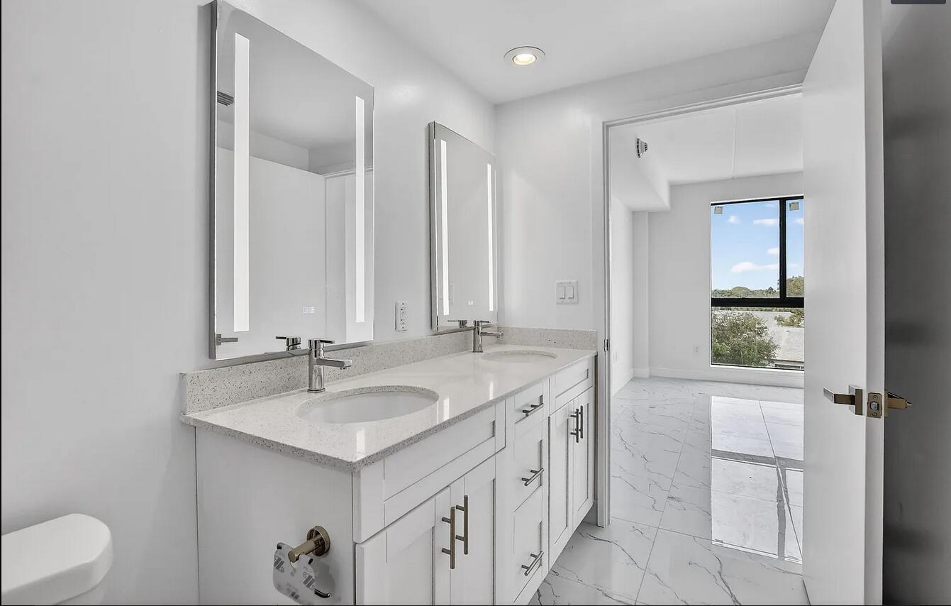 A modern bathroom features a double vanity with white cabinets, quartz countertops, and LED mirrors — 100 W Hidden Valley Boulevard # 302, Boca Raton FL 33487, BOCA RATON, FL