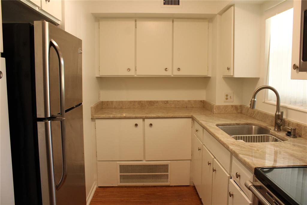 A kitchen features white cabinets, tan stone countertops, stainless steel appliances, and wood-look flooring — 3900 ROXANE BOULEVARD UNIT 10B, SARASOTA, FL