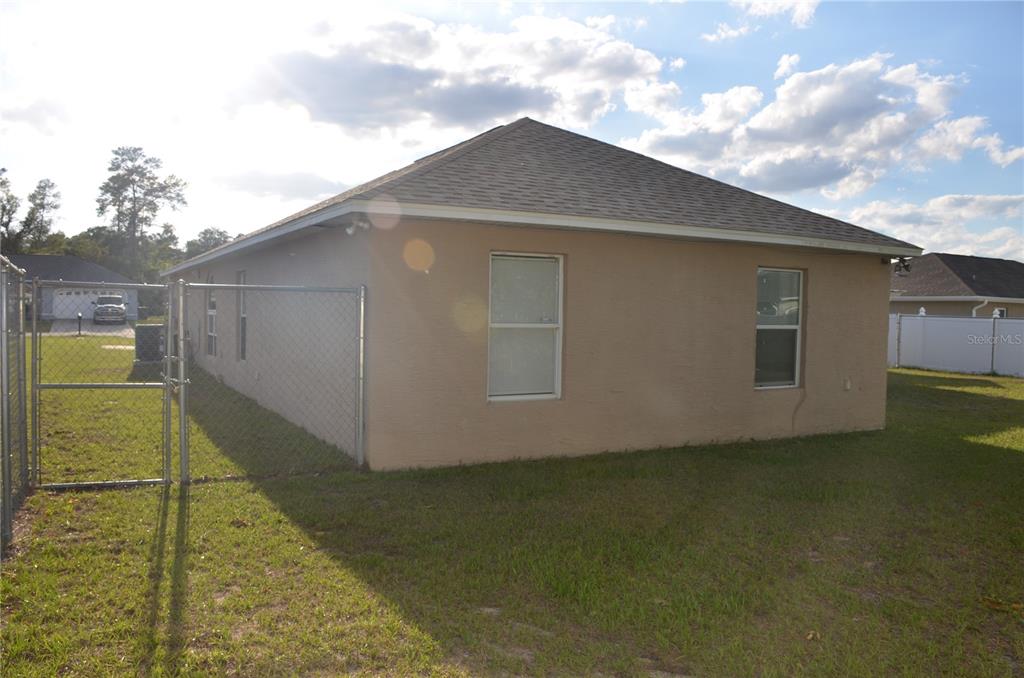 The exterior of a tan stucco house features a chain-link fence and two windows — 13785 SW 42ND COURT ROAD, OCALA, FL