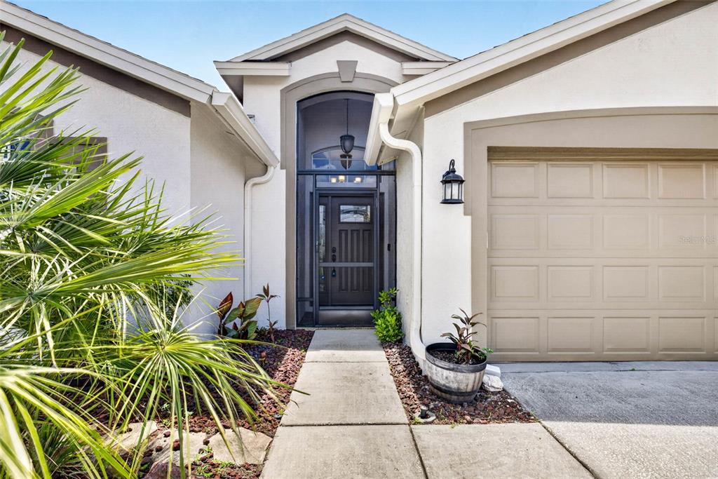 The exterior of a house features a tan garage door, a screened entryway, and landscaping — 29454 CROSSLAND DRIVE, WESLEY CHAPEL, FL