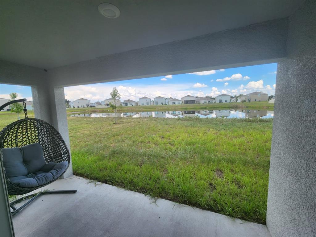 A covered patio overlooks a grassy backyard and a pond with houses in the distance — 16630 MOSAIC OAR DRIVE, WIMAUMA, FL