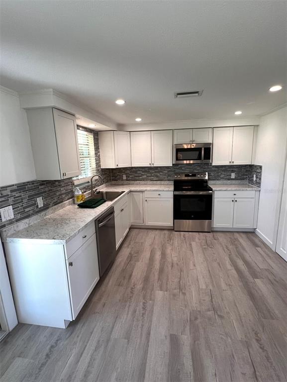 A kitchen features white cabinets, stainless steel appliances, gray stone backsplash, and wood-look flooring — 457 GARFIELD AVE NW AVENUE NW, PORT CHARLOTTE, FL