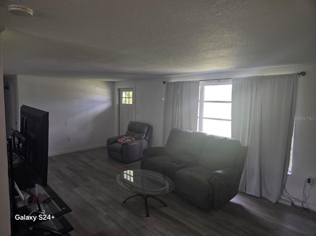 A living room features gray wood-look flooring, a dark sofa, a recliner, and a glass coffee table — 457 GARFIELD AVE NW AVENUE NW, PORT CHARLOTTE, FL