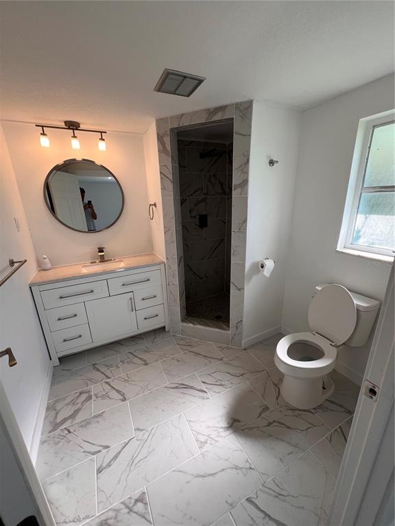 A bathroom features a white vanity, a round mirror, a tiled shower, and marble-patterned flooring — 457 GARFIELD AVE NW AVENUE NW, PORT CHARLOTTE, FL