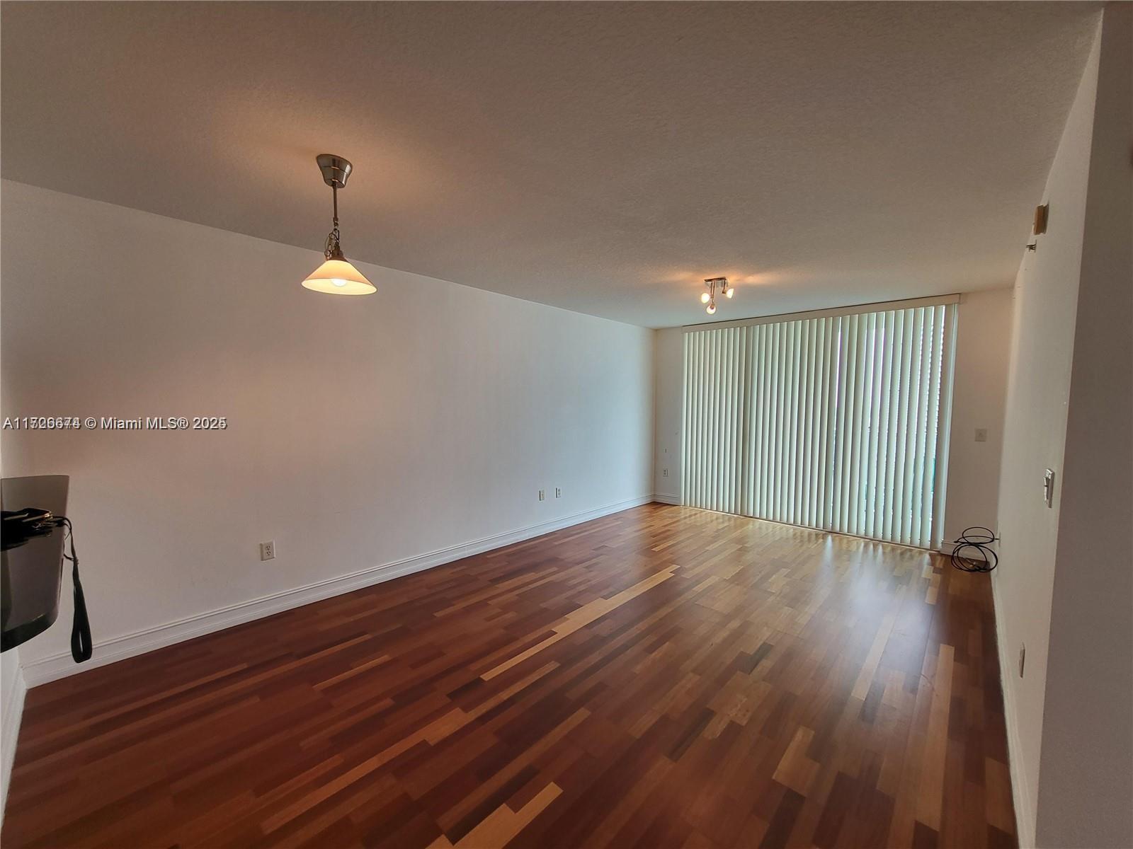 An empty room features hardwood flooring, white walls, a pendant light, and vertical window blinds — 31 SE 5th St # 2409, Miami FL 33131, MIAMI, FL