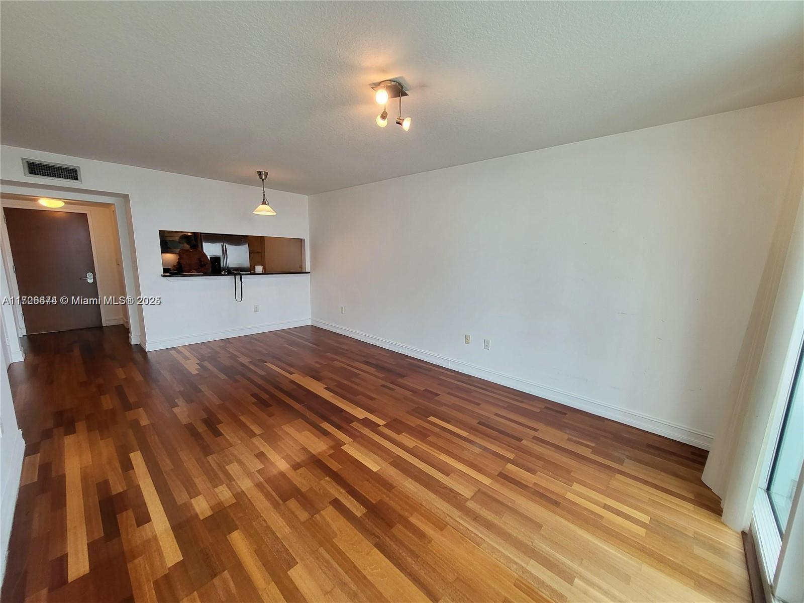 An empty living room features hardwood flooring, white walls, and a kitchen pass-through window — 31 SE 5th St # 2409, Miami FL 33131, MIAMI, FL