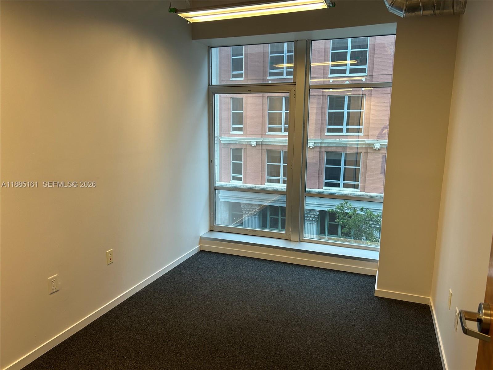 An empty office with dark carpet, white walls, and large windows overlooking a brick building — 14 NE 1st Ave # 500D, Miami FL 33132, MIAMI, FL