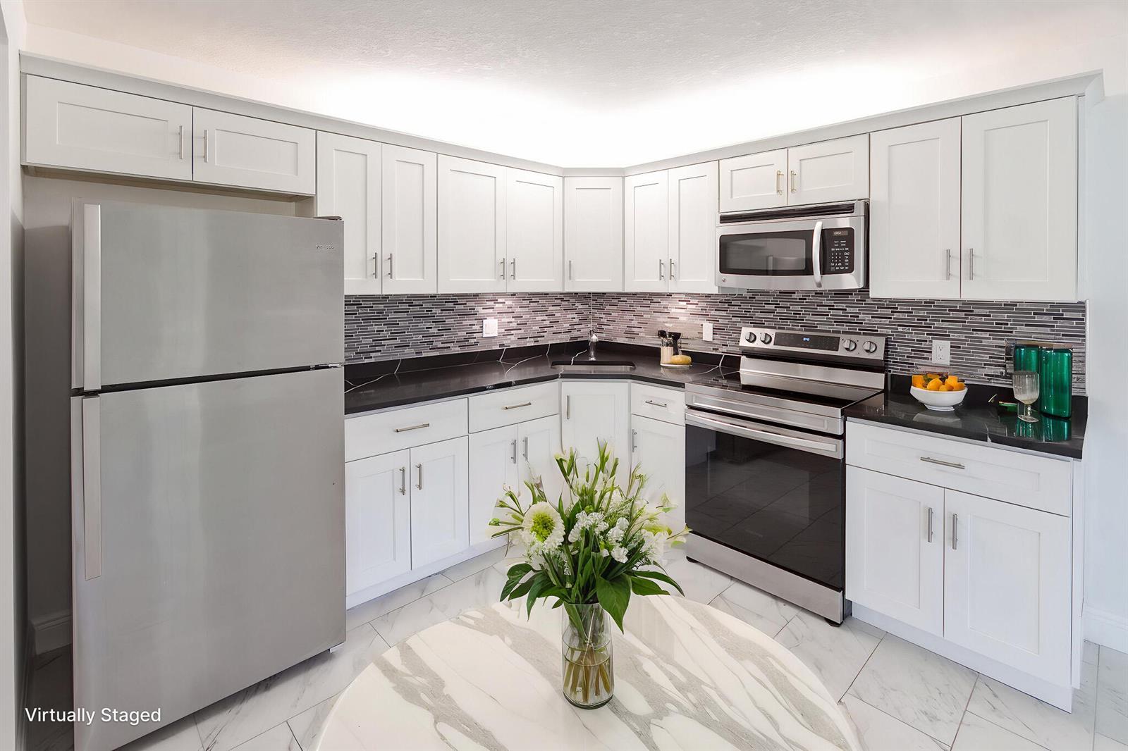 A kitchen with white cabinets, black countertops, stainless steel appliances, and a marble-topped table — 4899 Sable Pine Circle # A2, West Palm Beach FL 33417, WEST PALM BEACH, FL