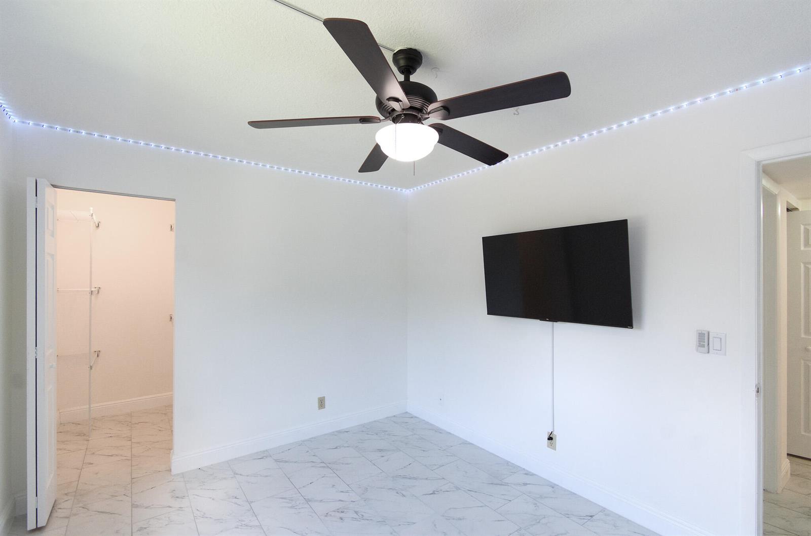 A bedroom with white walls, marble-style tile flooring, a ceiling fan, and a wall-mounted television — 4899 Sable Pine Circle # A2, West Palm Beach FL 33417, WEST PALM BEACH, FL