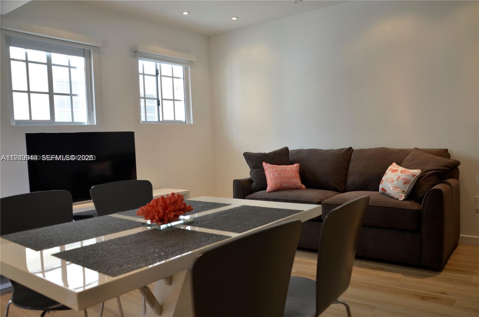 A dining area with a white table and chairs sits in front of a brown sofa — 700 16th St # 201, Miami Beach FL 33139, MIAMI BEACH, FL