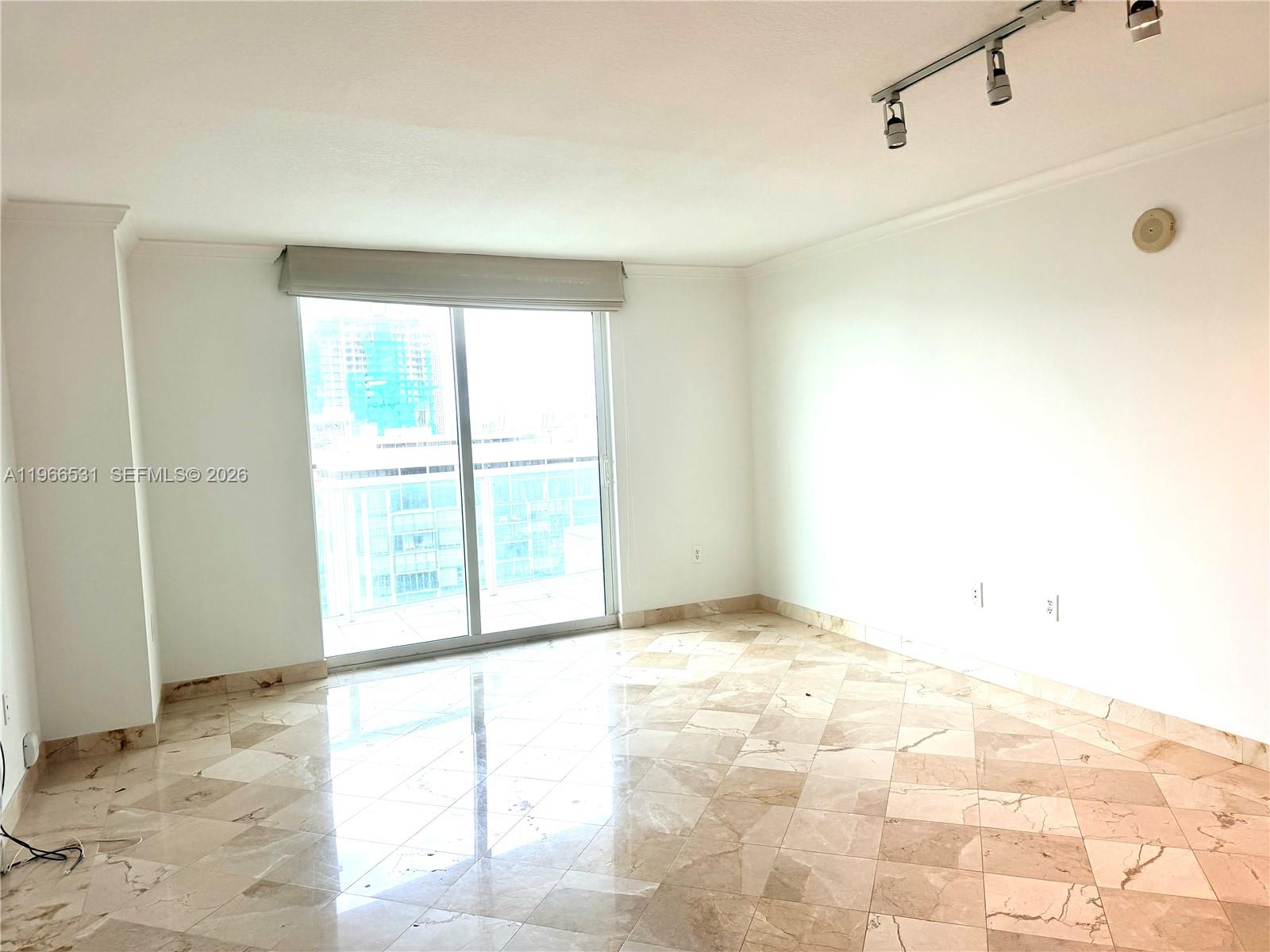 An empty room features beige marble tile flooring, white walls, and a sliding glass door — 2101 Brickell Ave # 2202, Miami FL 33129, MIAMI, FL