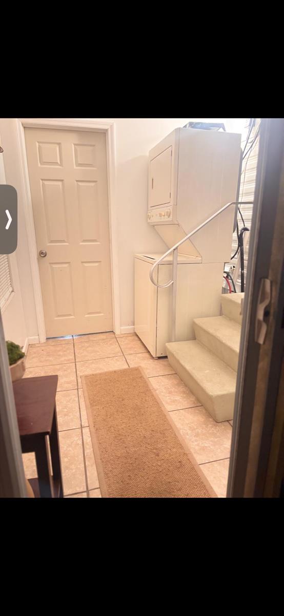 A laundry room features a stacked washer and dryer unit next to a carpeted staircase — 875 NE 48th Street # 186, Deerfield Beach FL 33064, DEERFIELD BEACH, FL