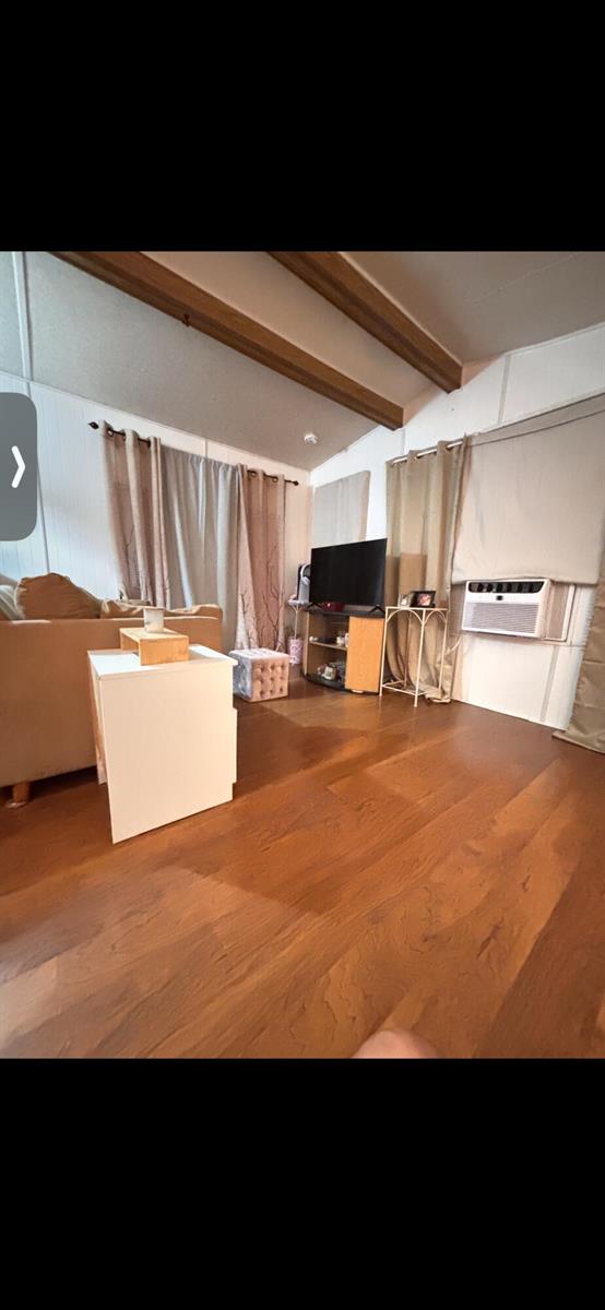 A living room features wood-look flooring, exposed ceiling beams, and a window-mounted air conditioner — 875 NE 48th Street # 186, Deerfield Beach FL 33064, DEERFIELD BEACH, FL