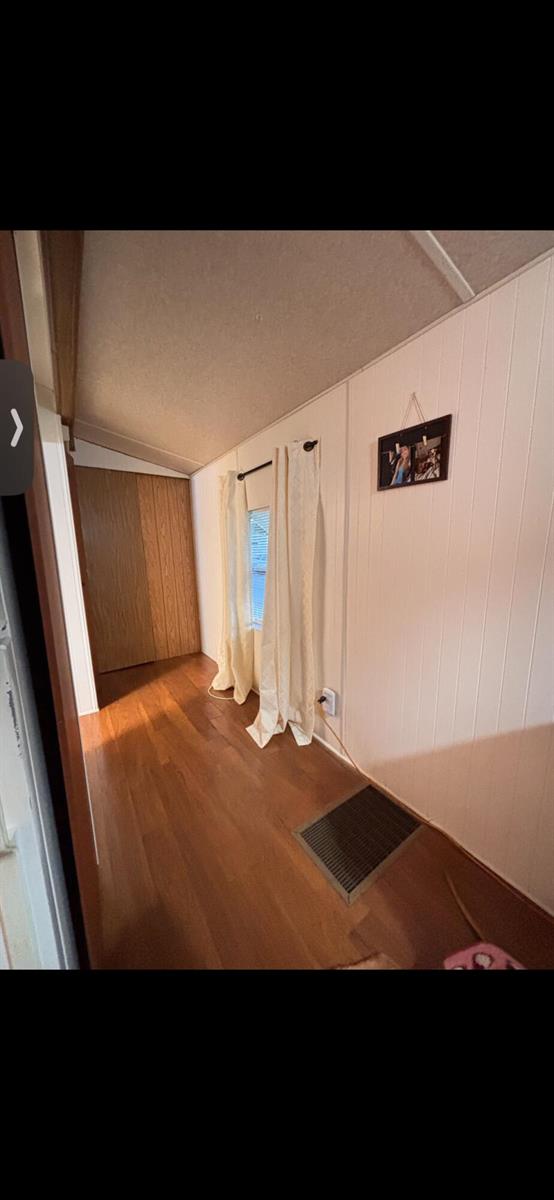 A narrow room with wood-look flooring, white paneled walls, a window with curtains, and a closet — 875 NE 48th Street # 186, Deerfield Beach FL 33064, DEERFIELD BEACH, FL
