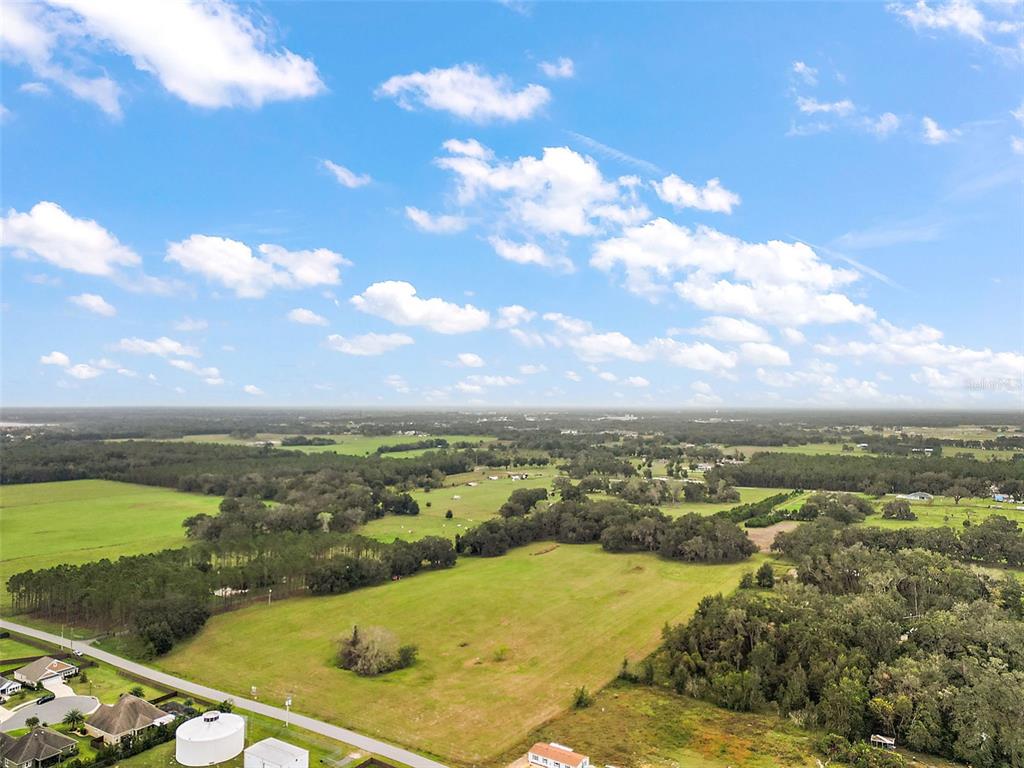 An aerial view shows a large, grassy field surrounded by trees and rural residential properties — SUMTER COUNTY ROAD 214, OXFORD, FL