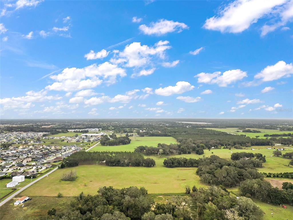 An aerial view shows a large grassy field bordered by trees and a residential neighborhood — SUMTER COUNTY ROAD 214, OXFORD, FL