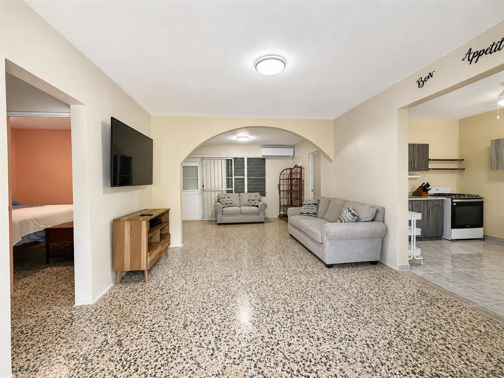 A living room with terrazzo floors, an arched entryway, a television, and an adjacent kitchen — 122 Pomarosa St. URB. SAN PEDRO, FAJARDO, PR
