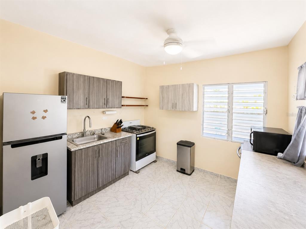 A kitchen features wood-grain cabinets, stainless steel appliances, light-colored tile floors, and a window — 122 Pomarosa St. URB. SAN PEDRO, FAJARDO, PR