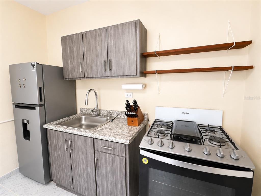 A kitchen features gray wood-grain cabinets, a stainless steel refrigerator, and a gas range — 122 Pomarosa St. URB. SAN PEDRO, FAJARDO, PR