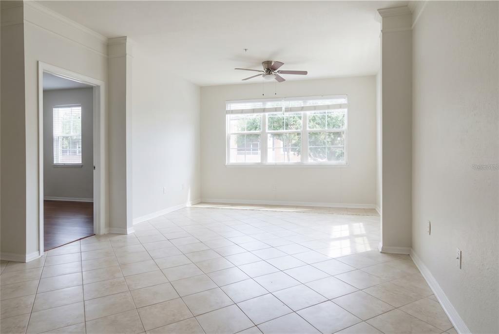 A bright, empty room features light-colored tile flooring, a ceiling fan, and large windows — 3344 CORONA VILLAGE WAY UNIT 205, ORLANDO, FL