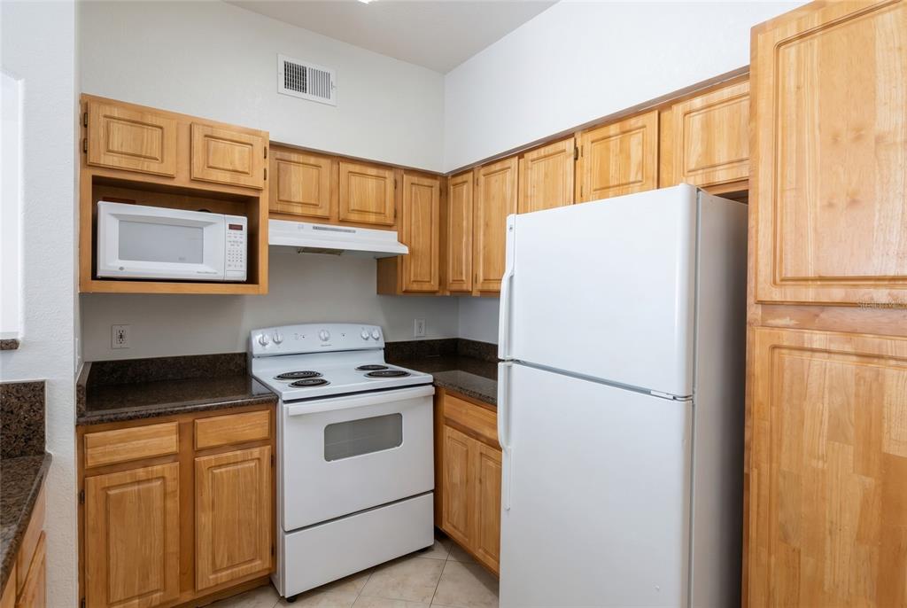 A kitchen features light wood cabinets, dark granite countertops, and white appliances — 3344 CORONA VILLAGE WAY UNIT 205, ORLANDO, FL