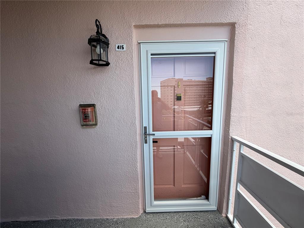 An exterior view of a door numbered 415 with a storm door and wall-mounted light — 6025 SHORE BOULEVARD S UNIT 415, GULFPORT, FL