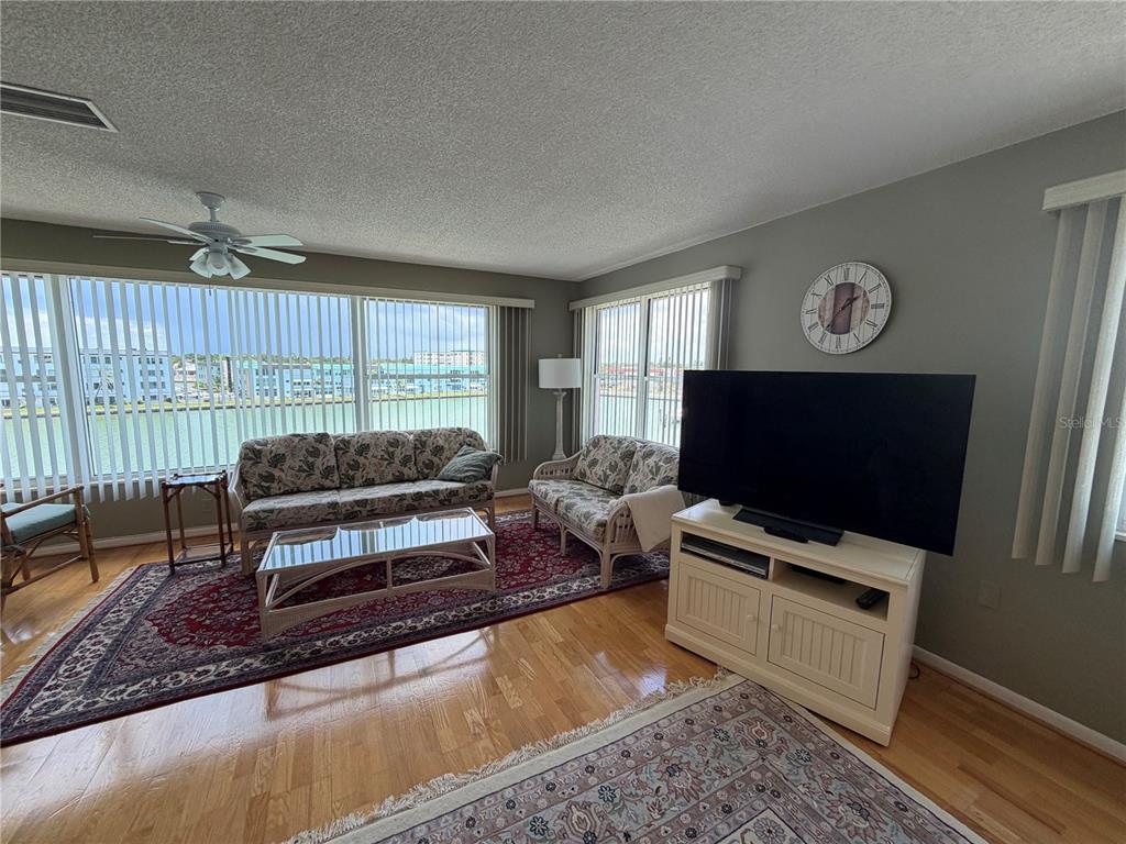 A living room with hardwood floors, a large area rug, and floor-to-ceiling windows overlooking water — 6025 SHORE BOULEVARD S UNIT 415, GULFPORT, FL